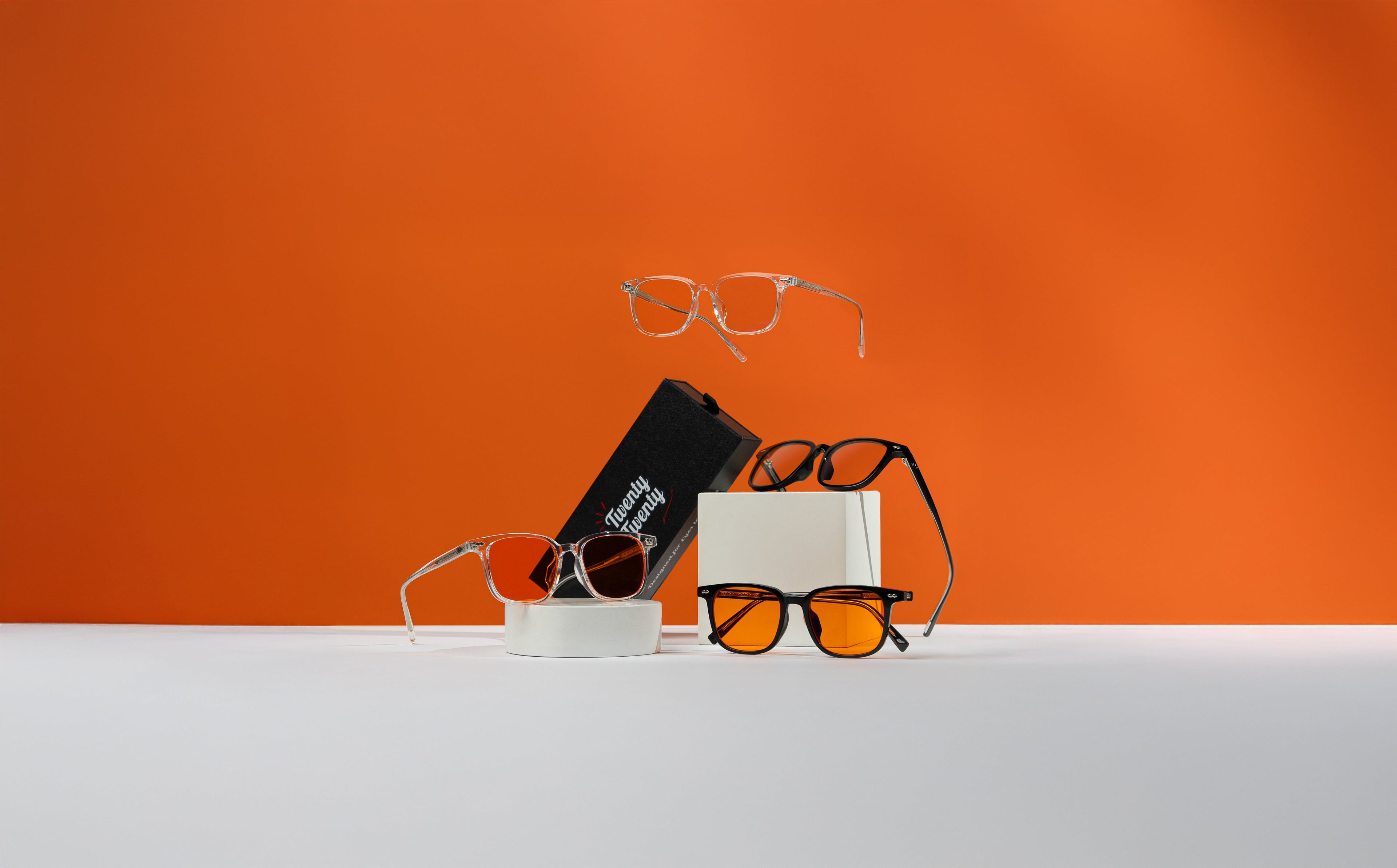 Eyeglasses and sunglasses displayed on a white surface with an orange background